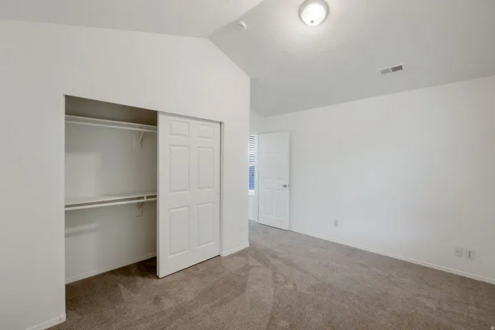 Bedroom featuring vaulted ceilings, plush carpet flooring, a bifold closet with shelving and hanging rods, and a white paneled door