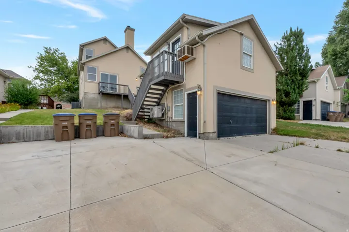 Exterior stucco siding with a prominent black garage door, a private exterior staircase leading to an upper-level balcony, and an additional exterior access door