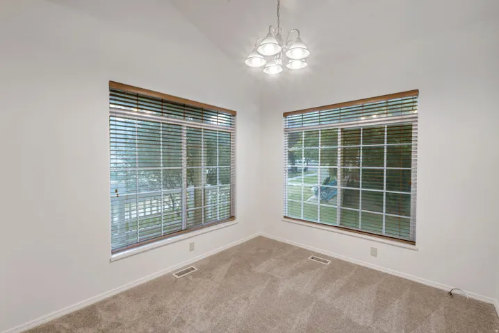 Vaulted ceiling room featuring two large windows with horizontal blinds and wood-finish trim, a five-light chandelier, and carpeted flooring