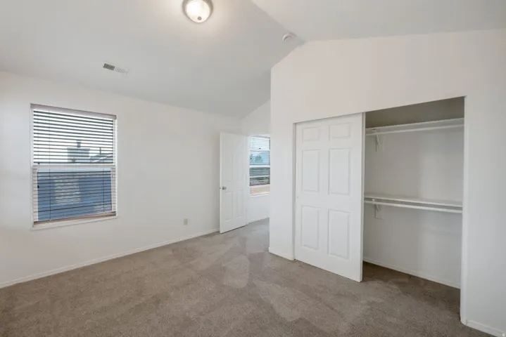 Carpeted room featuring a vaulted ceiling and a window with blinds