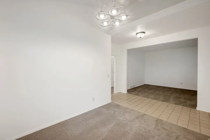 Spacious interior room with neutral-toned carpeting, a contemporary ceiling light fixture, and white wall finishes