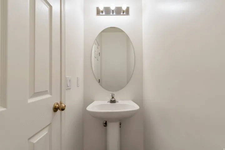 Pedestal sink with a polished chrome faucet, an oval mirror, and a three-light vanity fixture