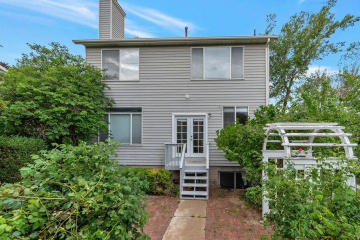 Rear exterior featuring light gray siding, multiple windows, a two-story structure, and a ground-level patio with brick paving