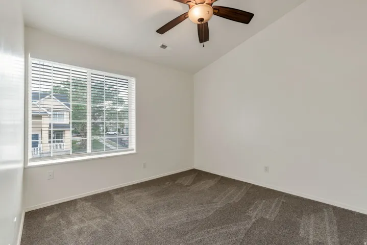 Carpeted room featuring a large window with white blinds, a ceiling fan with integrated lighting, and white baseboards