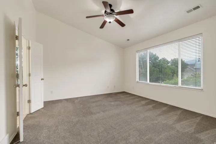 Spacious room featuring vaulted ceilings, a ceiling fan with integrated lighting, and neutral-toned carpeting
