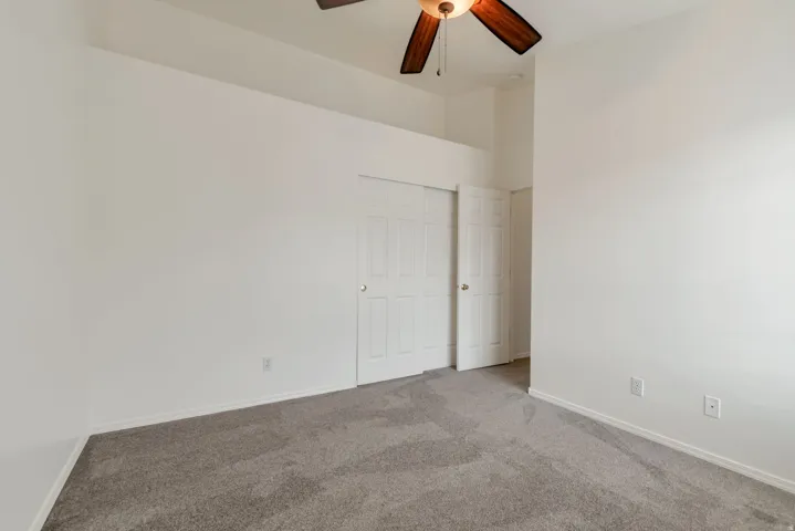 Spacious room featuring neutral carpet flooring, white walls, a ceiling fan with integrated lighting, and a closet with bifold doors
