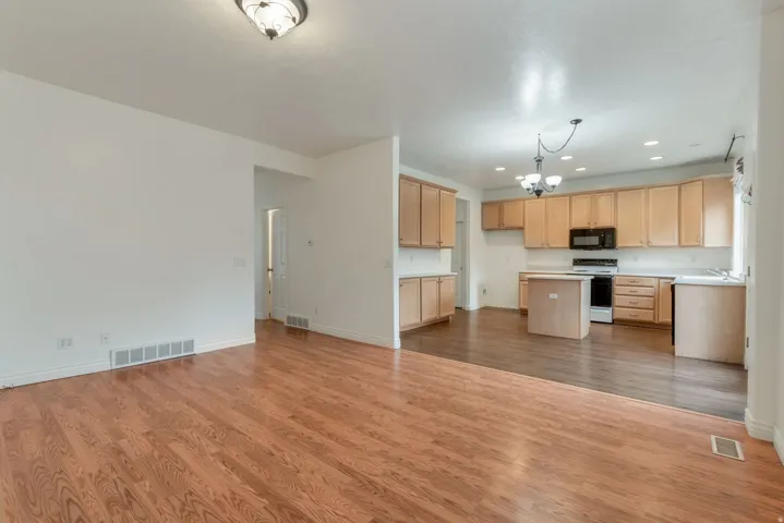 Open-concept living area featuring wood-finish flooring and a kitchen with light wood cabinetry, a central island, and black appliances