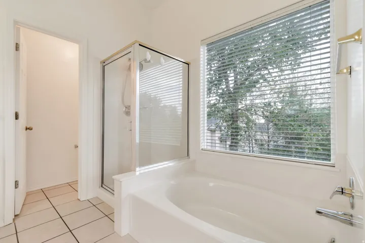 Bathroom featuring a built-in bathtub with a window, a glass-enclosed shower, and tile flooring
