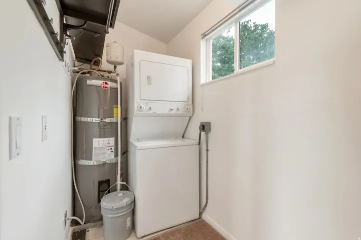 Dedicated laundry area featuring a stacked washer and dryer, water heater, and an upper window providing natural light