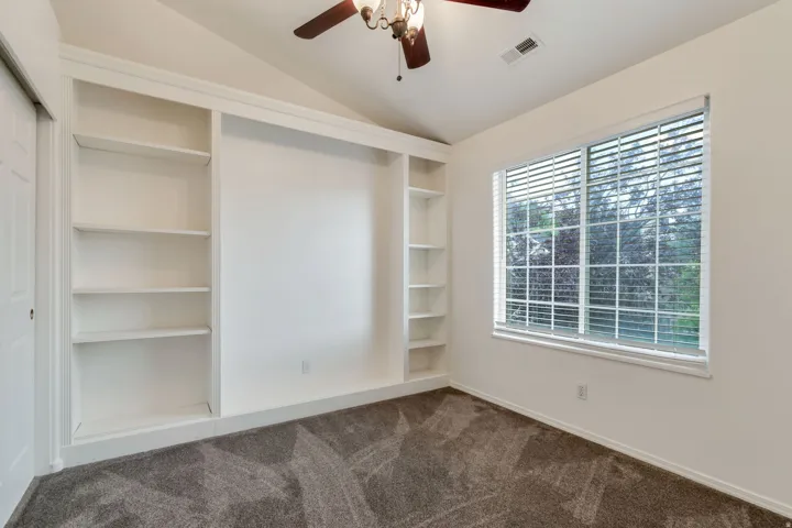Room featuring built-in white shelving, vaulted ceiling, and a ceiling fan with integrated lighting