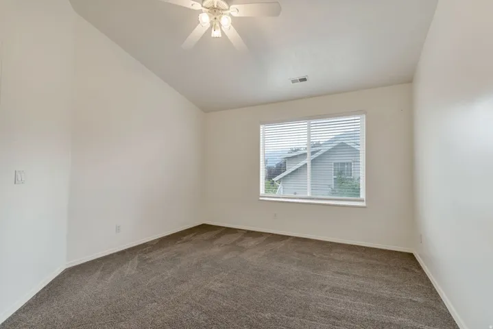 Spacious room featuring vaulted ceilings, neutral-toned carpeting, a ceiling fan with integrated lighting, and a large window with white blinds