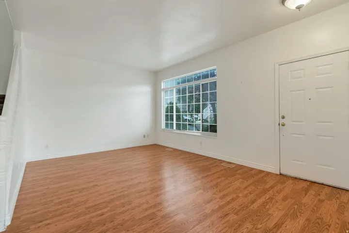 Spacious room featuring wood-finish flooring, white walls, and a large multi-pane window with blinds