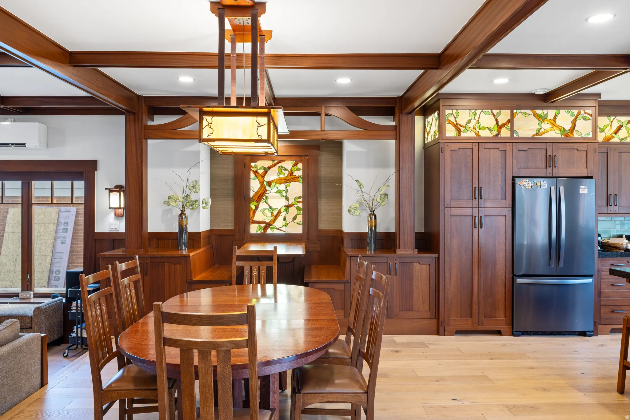 Dining area featuring wood-finish flooring, exposed wood beam ceiling, and a built-in banquette with custom stained-glass accents