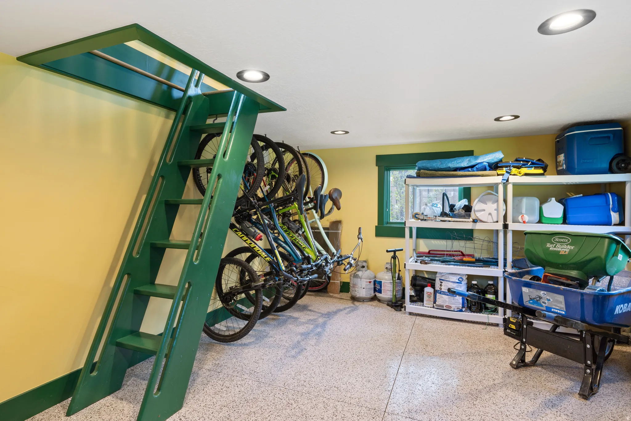 Dedicated storage area featuring a green built-in ladder system, recessed ceiling lighting, a window with green trim, and a durable speckled floor finish