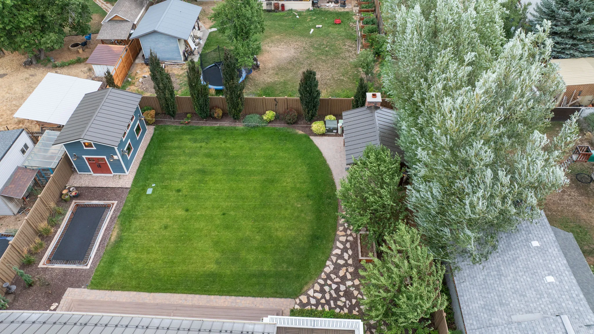 Expansive backyard featuring a manicured lawn, a rectangular covered pool, and a blue detached shed with a red door