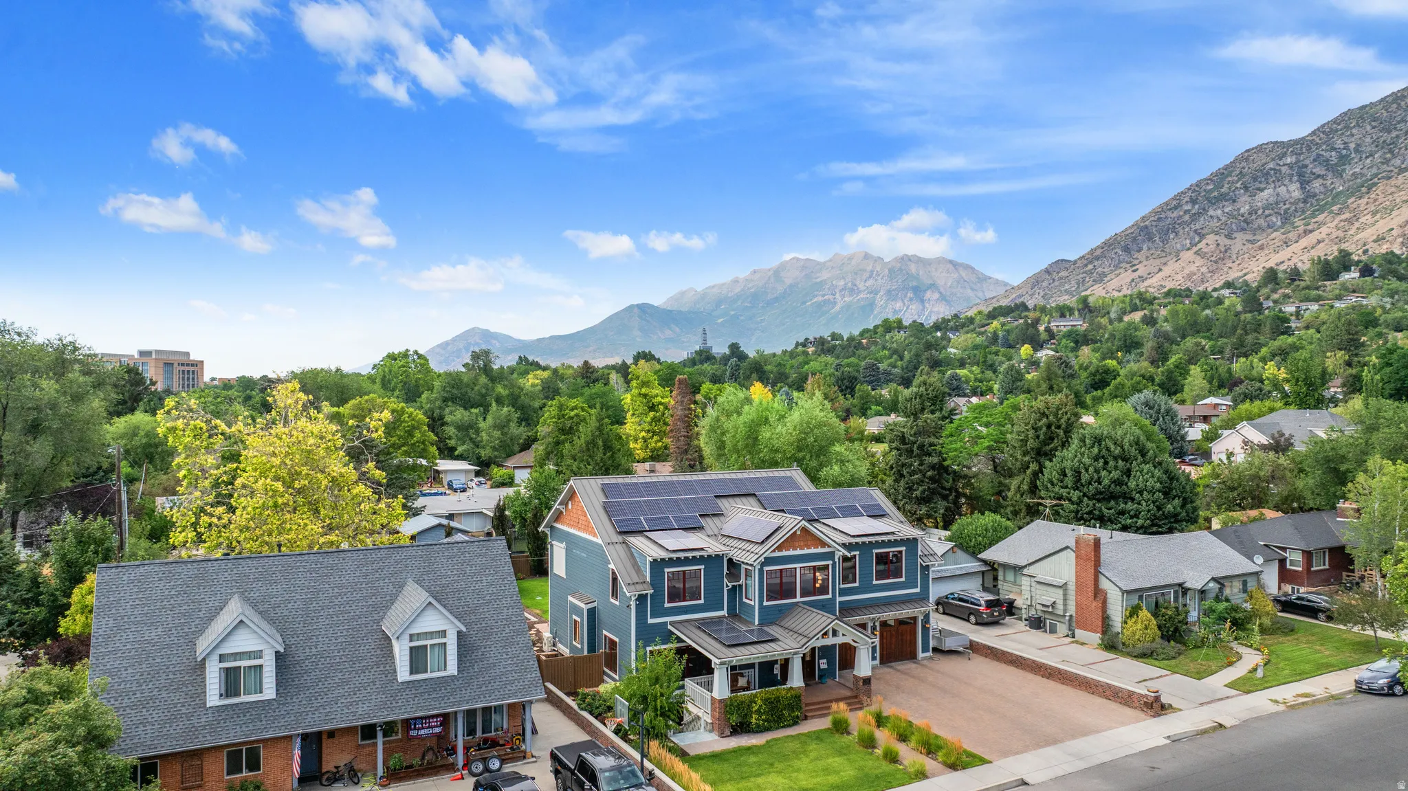 Two-story residence featuring a blue exterior with brown trim accents, multiple solar panel arrays, a covered front porch, and an attached two-car garage