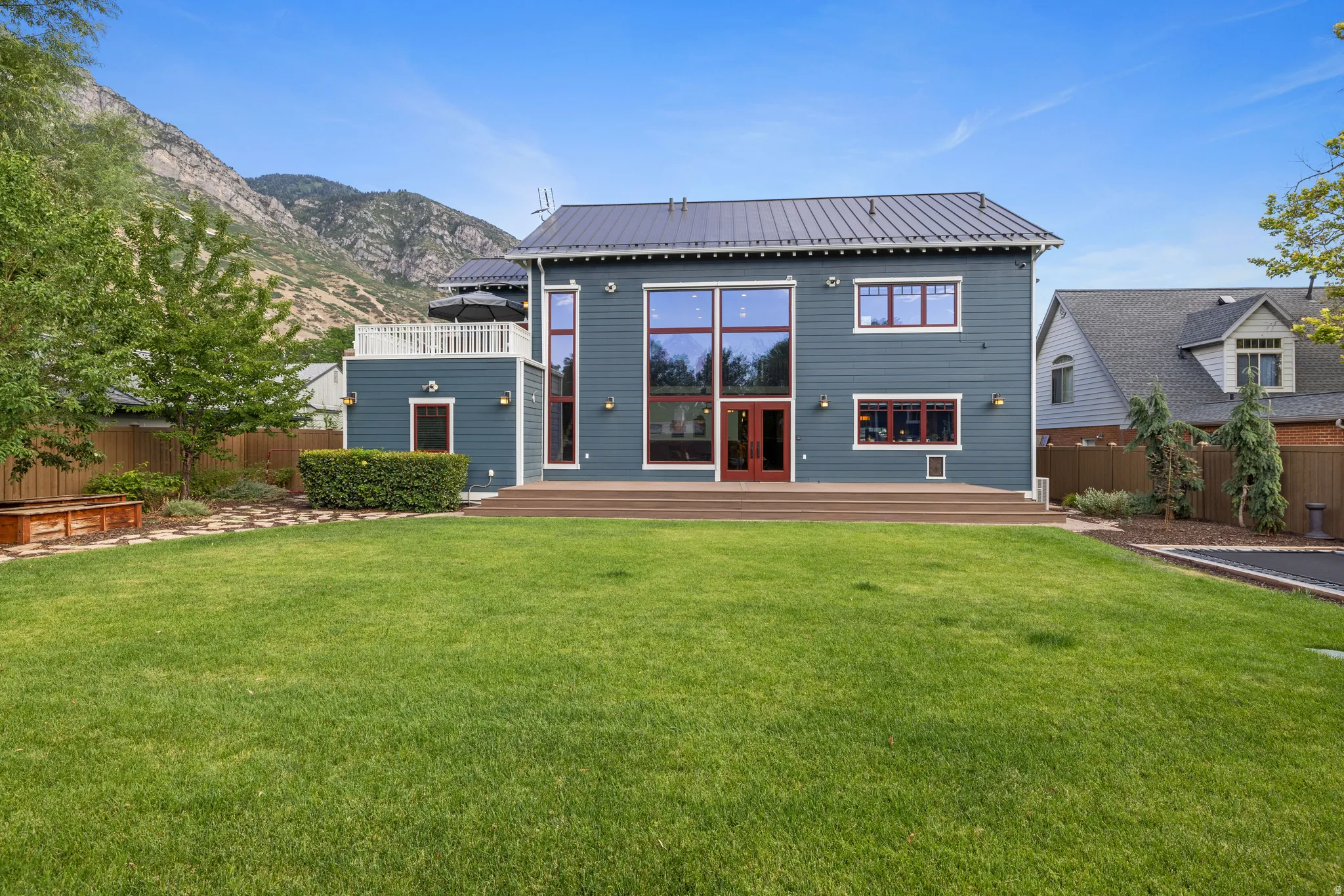 Rear exterior featuring a metal roof, expansive lawn, multi-level wood deck, floor-to-ceiling windows, and a second-story terrace with white railings