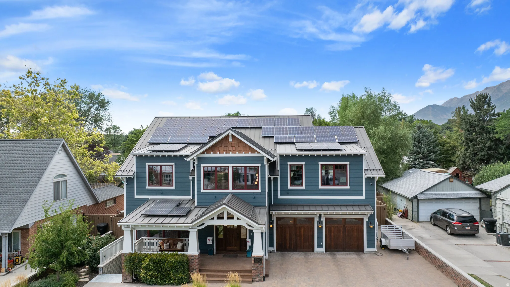 Modern residence featuring multiple solar panels, a covered front porch, and a two-car garage with wood-finish doors