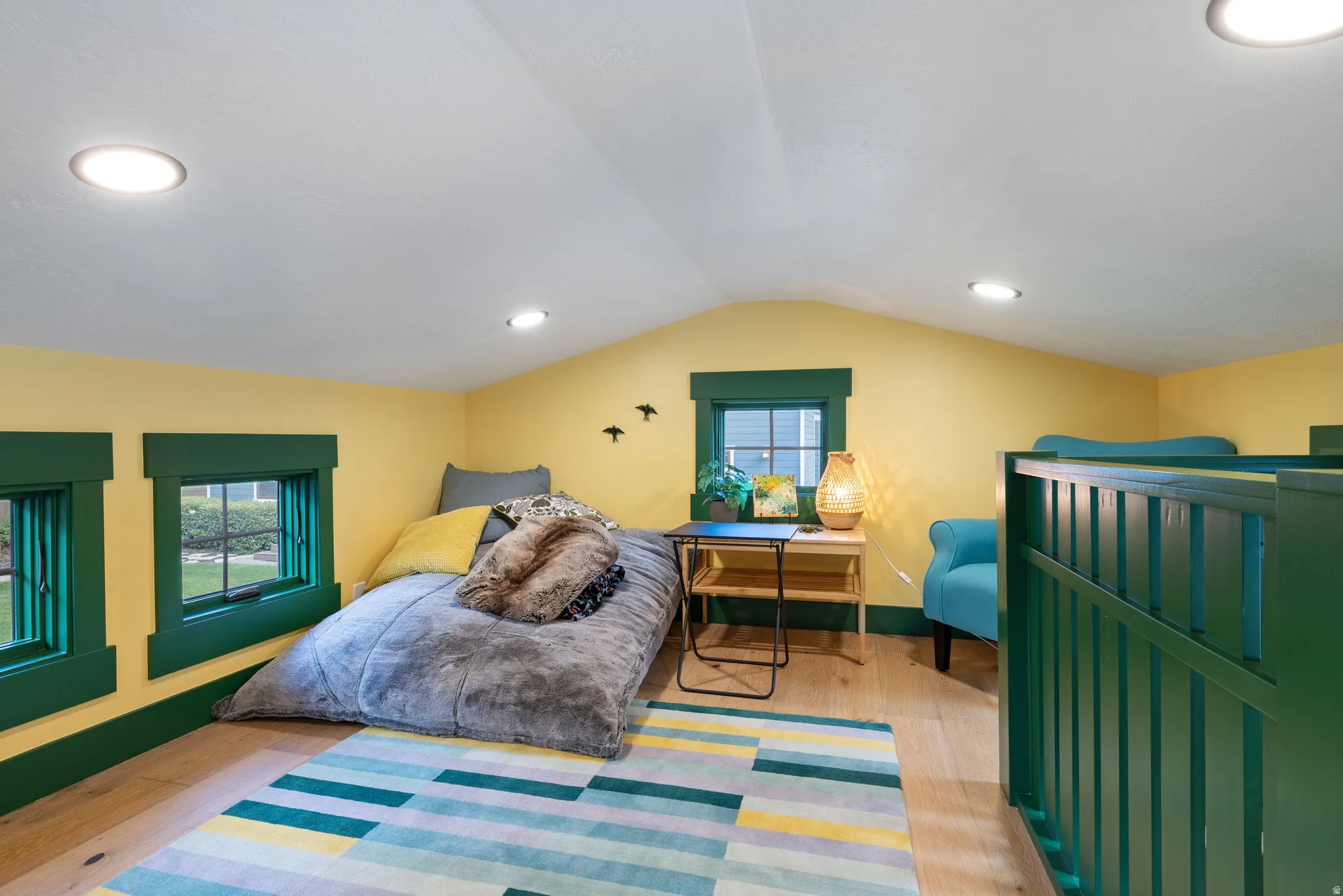 Brightly colored loft featuring light wood-finish flooring, recessed lighting, and multiple windows with deep green trim