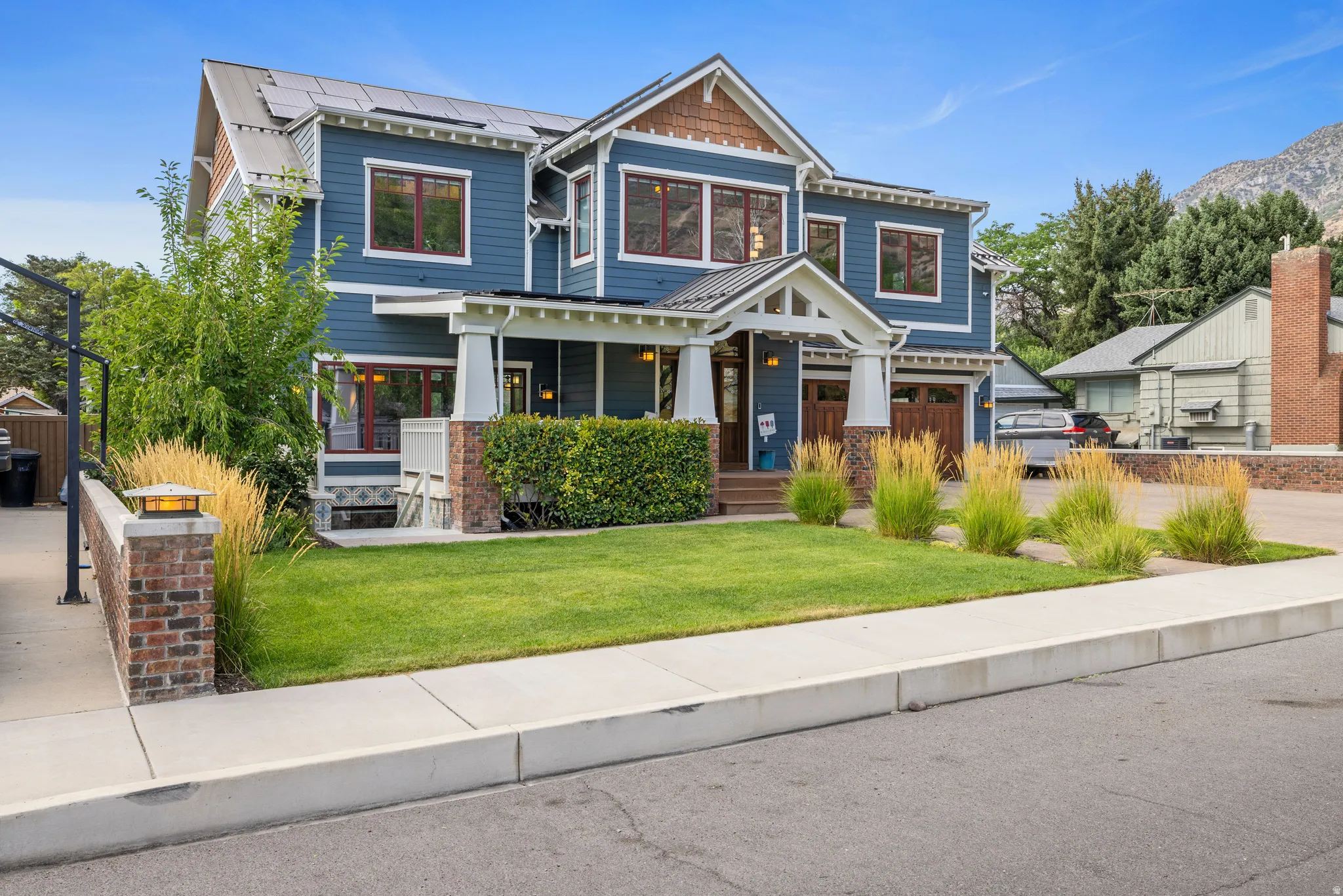 Two-story residence featuring a blue siding exterior with red window frames, a welcoming covered front porch, and an attached two-car garage with wood-finish doors