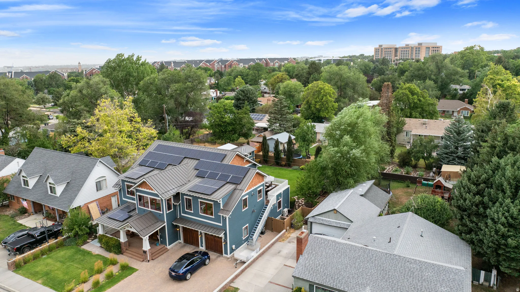 Contemporary multi-level residence featuring a blue siding exterior, multiple solar panel arrays, and a covered front porch entry