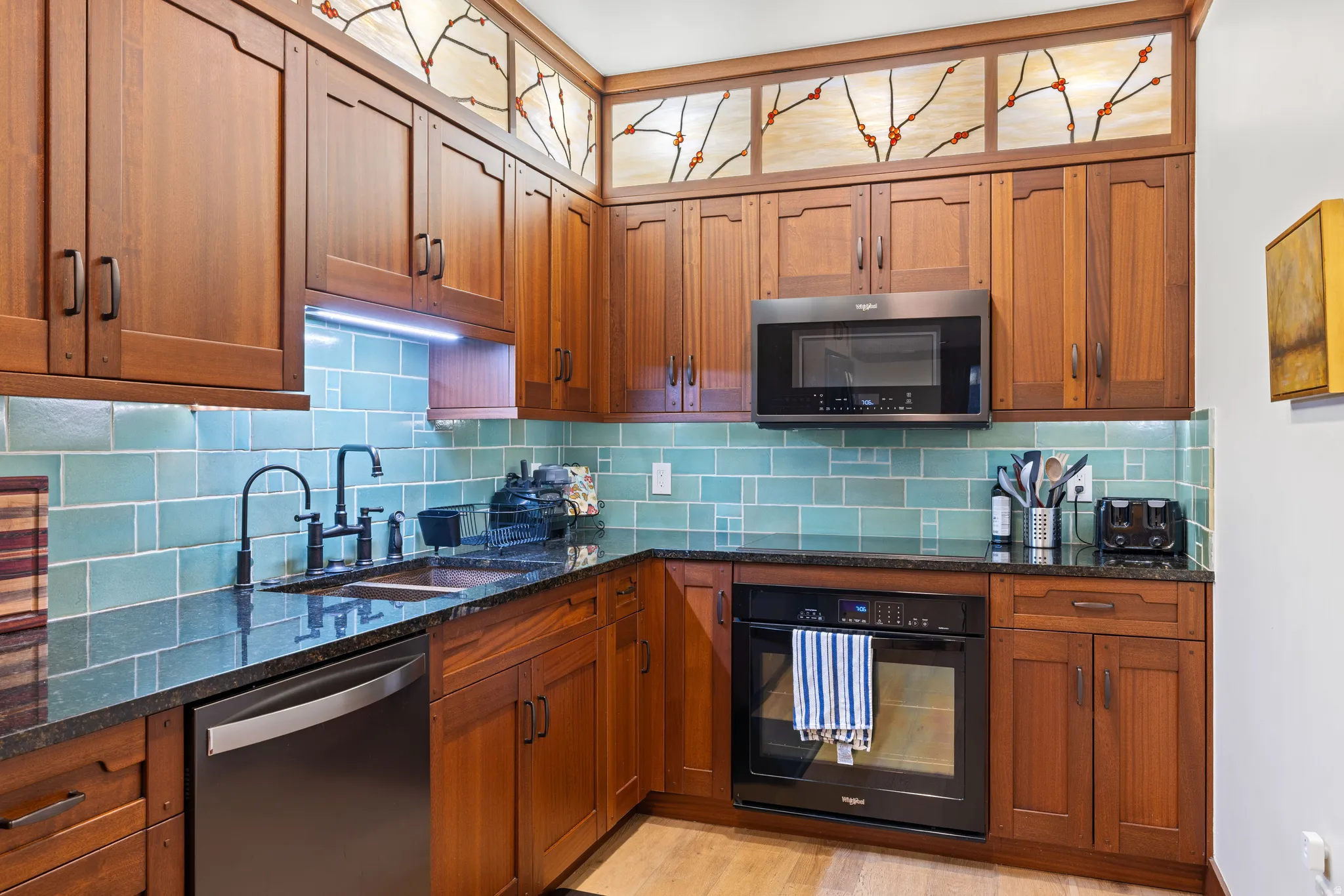 Kitchen featuring custom wood cabinetry with stained glass accents, a black appliance package, and an aqua subway tile backsplash