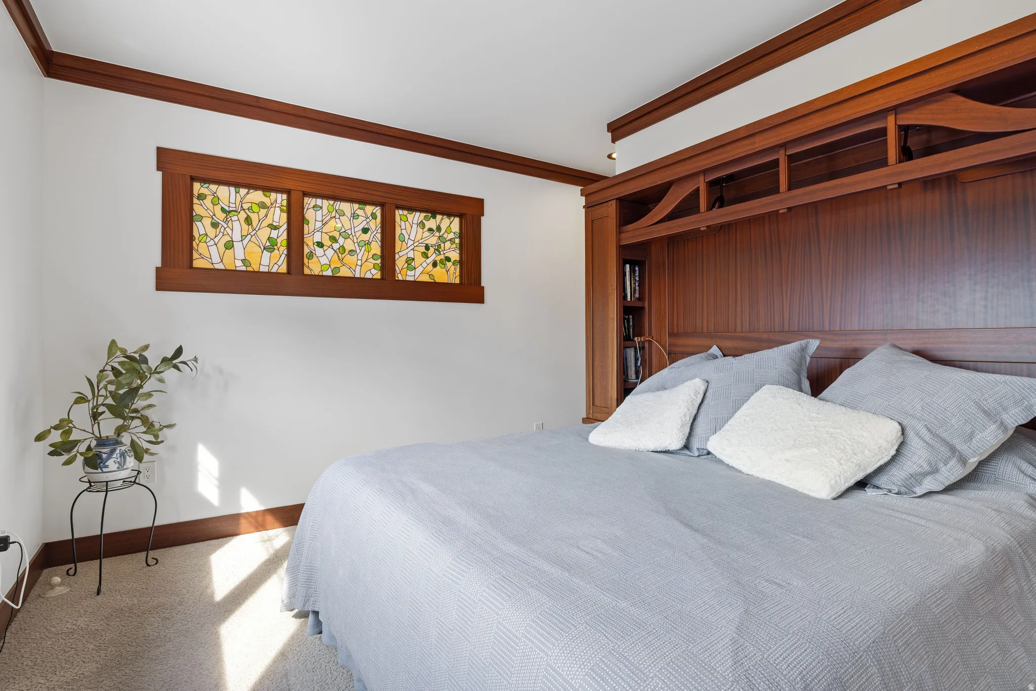 Primary bedroom featuring a built-in wooden headboard with integrated shelving, hardwood trim, and a decorative stained glass transom window