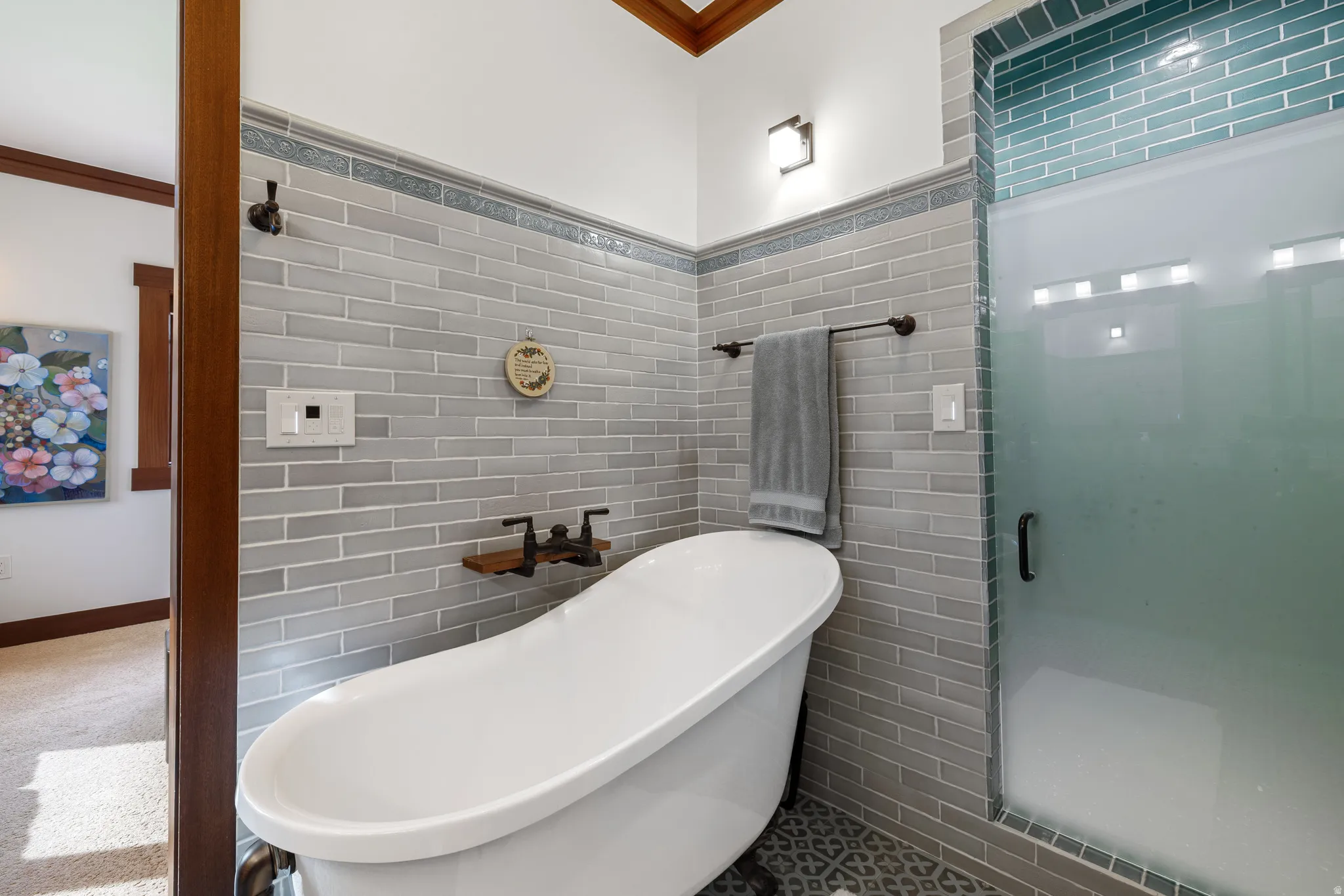 Freestanding soaking tub with dark-finish hardware, subway tile surround, patterned floor tile, and a frosted glass shower enclosure