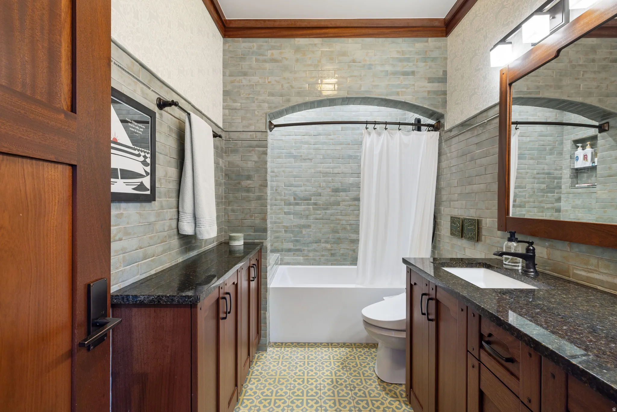 Full bathroom featuring wood-finish cabinetry with dark countertops, a white porcelain sink, and a combination tub and shower with subway tile surround