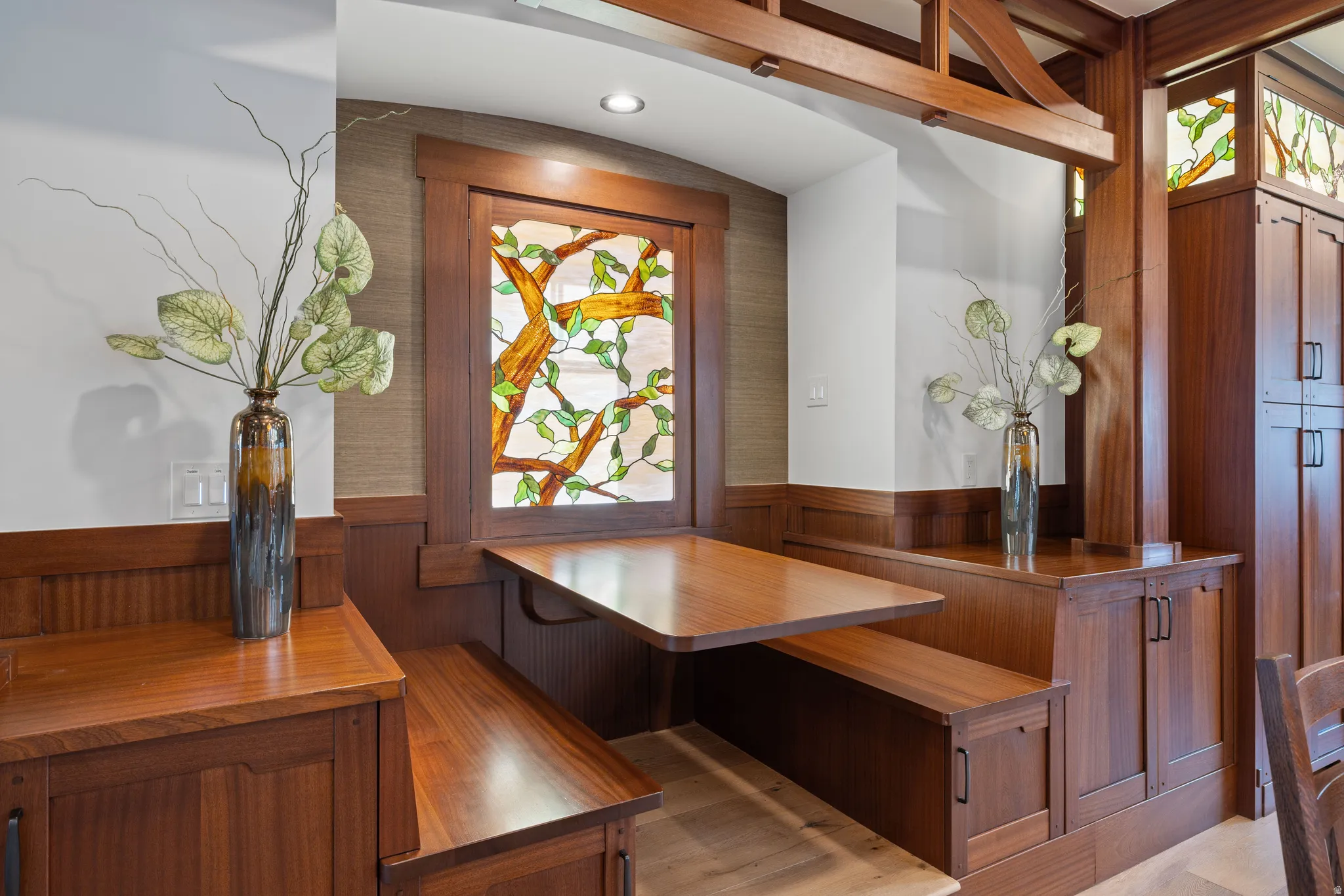 Built-in dining nook featuring rich wood-finish trim, banquette seating, a fixed table, stained glass window, and integrated cabinetry