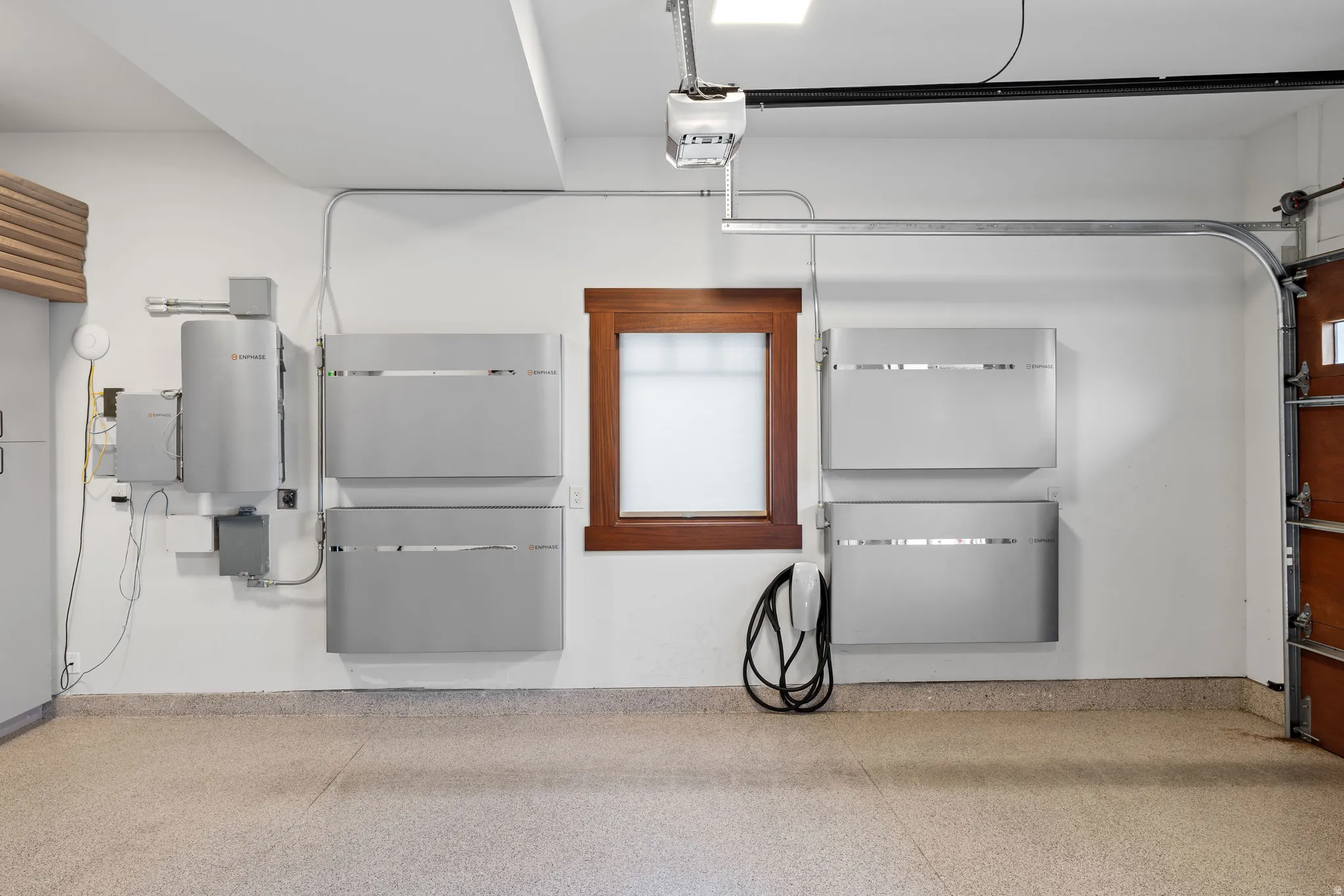 Garage space featuring an epoxy-coated concrete floor, a wood-framed window, modern wall-mounted energy storage units, an electric vehicle charging station, and an automatic garage door opener