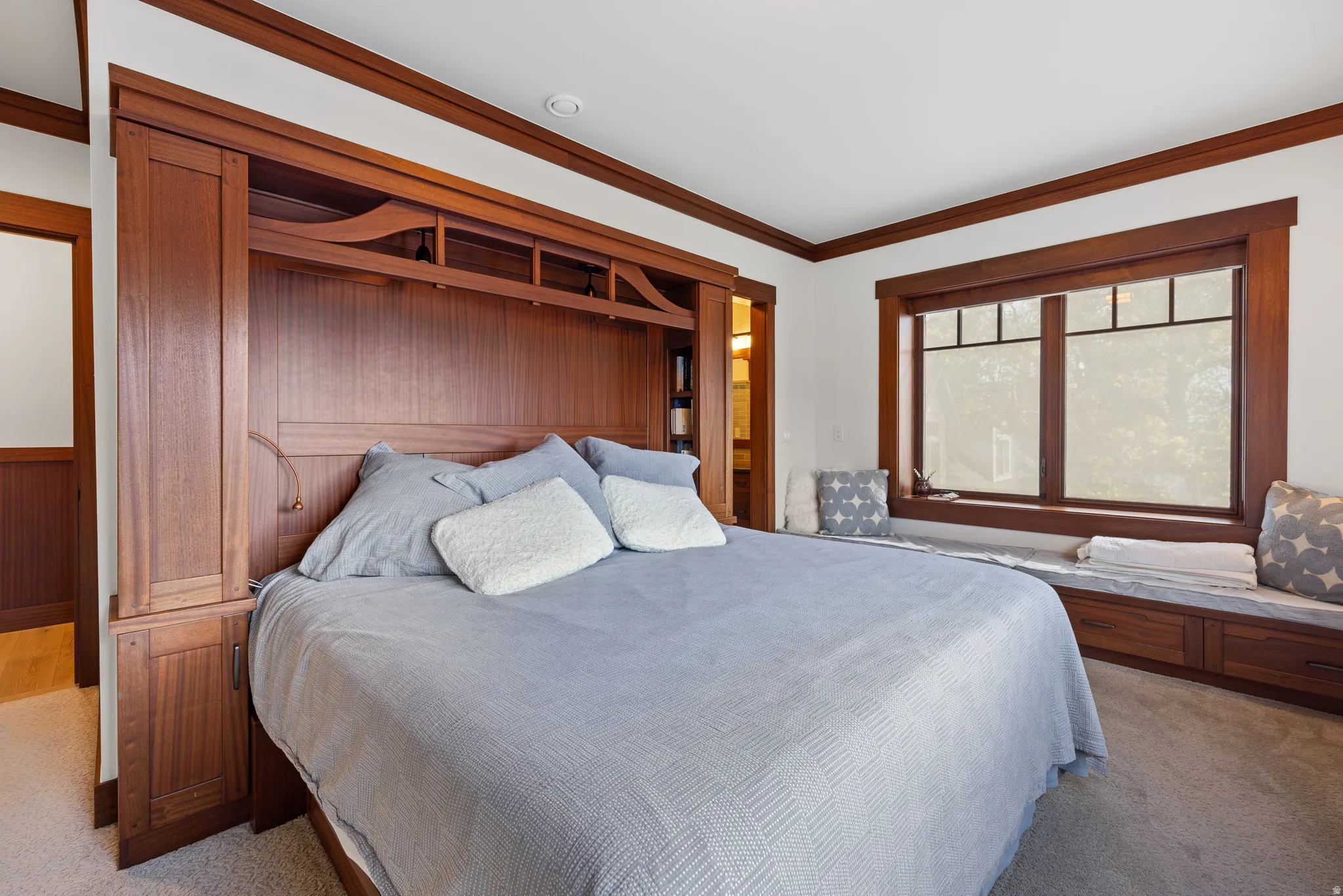 Primary bedroom featuring a built-in wooden bed frame with integrated cabinetry and shelving, a window with dark wood trim and grid detailing, and a built-in window seat with storage drawers
