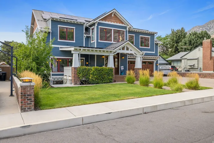 Two-story residence featuring a blue siding exterior with red window frames, a welcoming covered front porch, and an attached two-car garage with wood-finish doors