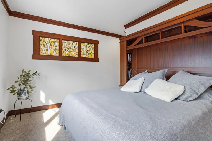 Primary bedroom featuring a built-in wooden headboard with integrated shelving, hardwood trim, and a decorative stained glass transom window