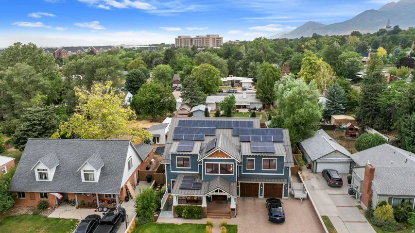 Contemporary multi-story residence featuring a blue exterior with wood-finish accents, multiple solar panels, an integrated two-car garage, and a covered front porch