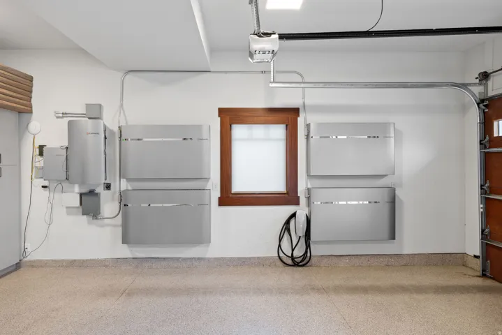Garage space featuring an epoxy-coated concrete floor, a wood-framed window, modern wall-mounted energy storage units, an electric vehicle charging station, and an automatic garage door opener