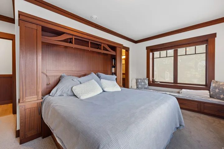 Primary bedroom featuring a built-in wooden bed frame with integrated cabinetry and shelving, a window with dark wood trim and grid detailing, and a built-in window seat with storage drawers