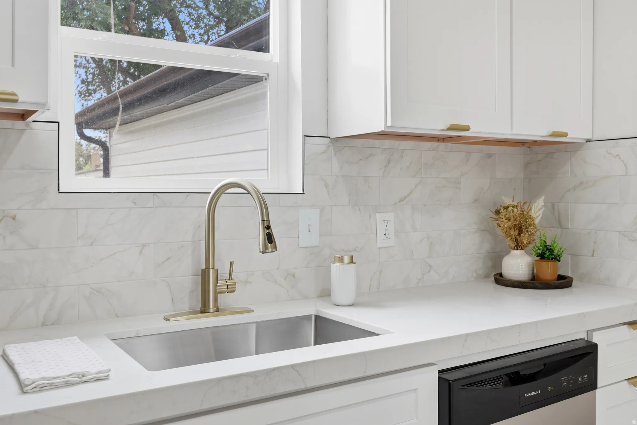 Kitchen workstation featuring a stainless steel undermount sink, brushed nickel high-arc faucet, white countertops, and a subway tile backsplash