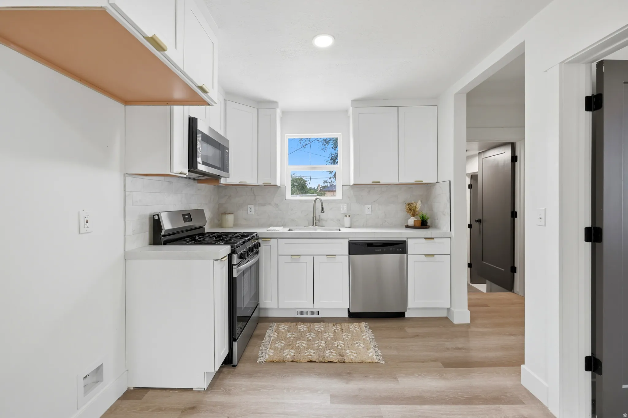 Bright kitchen featuring white cabinetry with gold-tone hardware, stainless steel appliances, and a tile backsplash