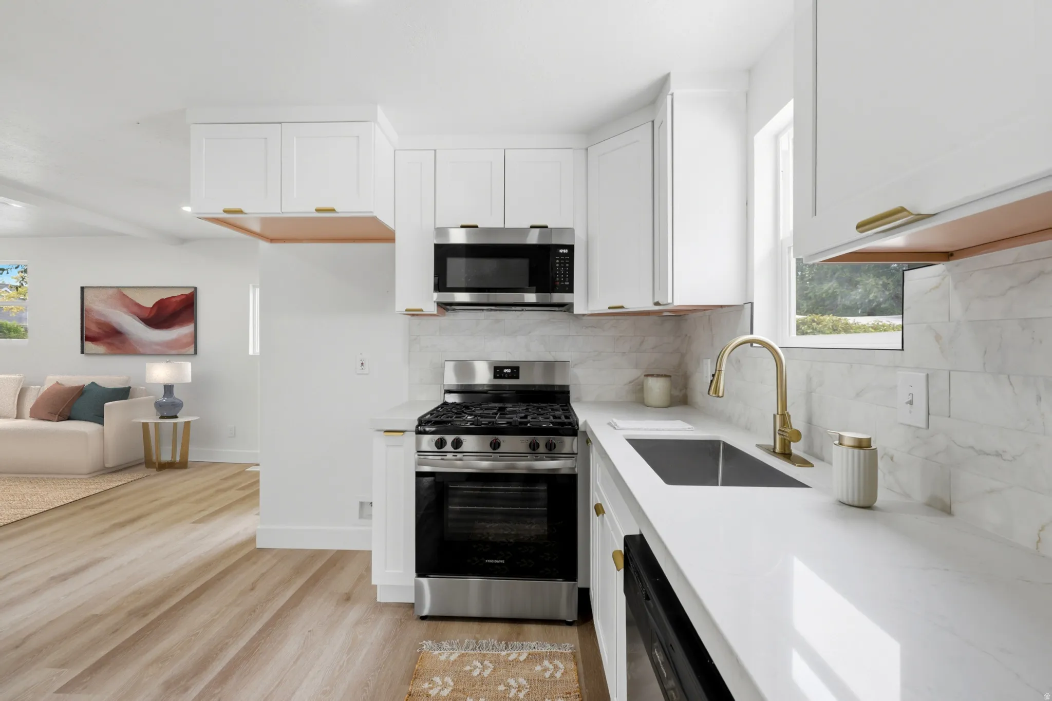 Modern kitchen featuring white cabinetry with gold-tone hardware, stainless steel appliances, a white countertop, and a light-toned tile backsplash