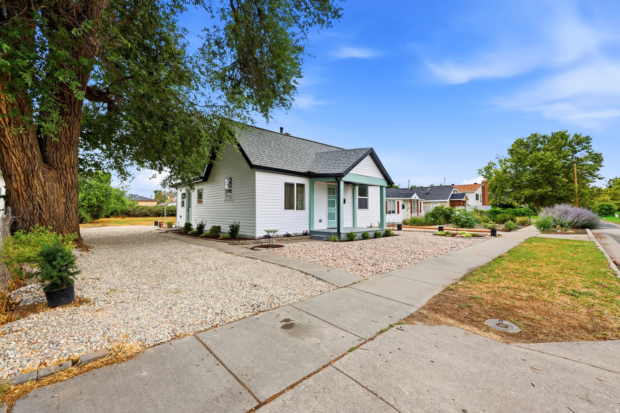 White siding home with a welcoming covered porch, dark shingle roof, and a meticulously graveled front yard