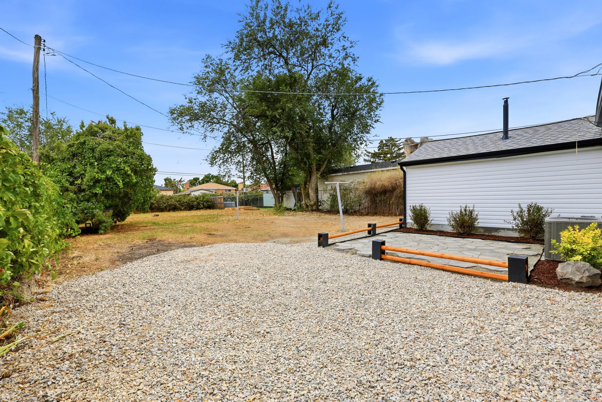 Expansive gravel parking area with a stone patio and shrub landscaping