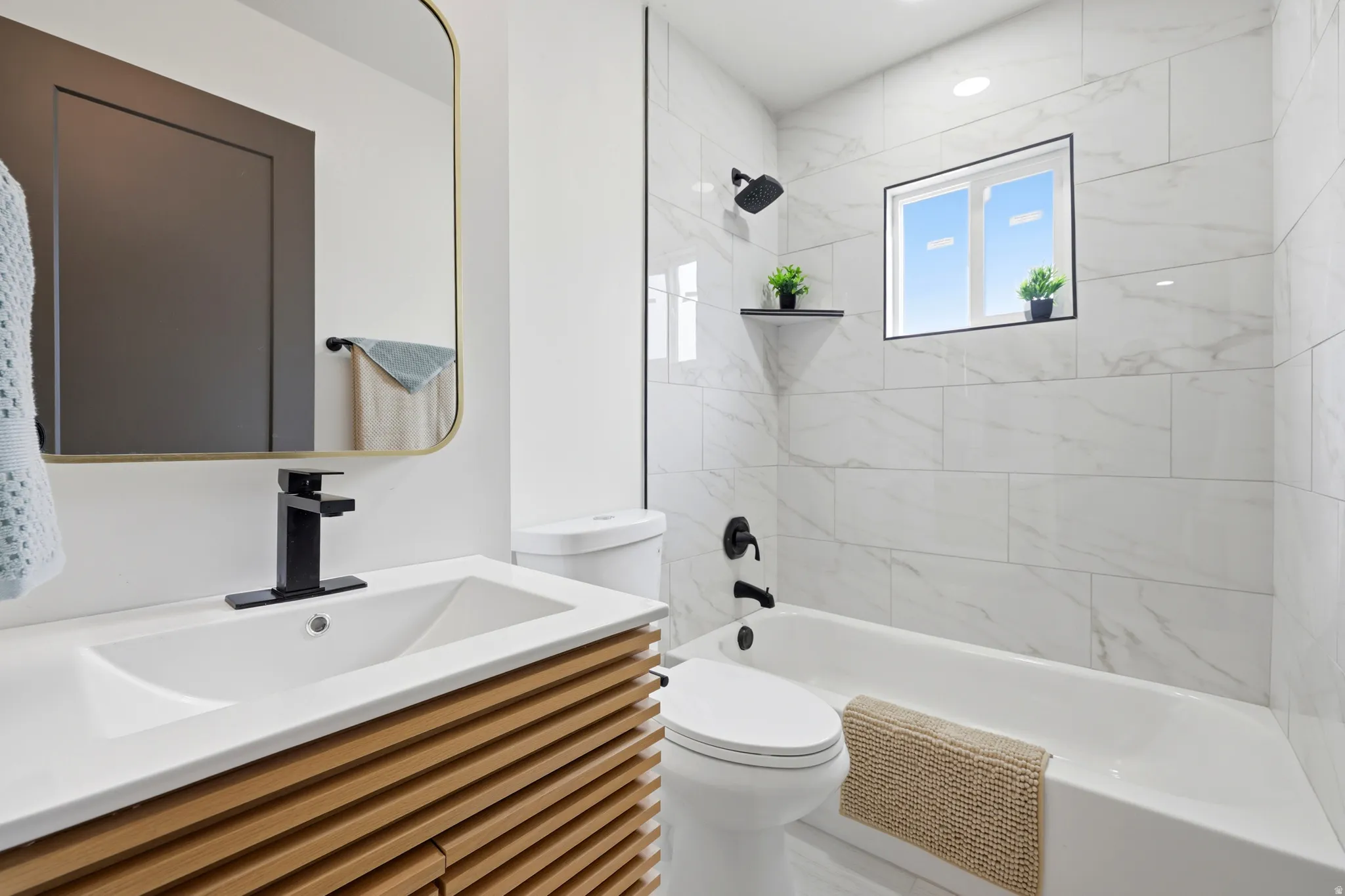 Contemporary bathroom featuring a slatted wood-finish vanity, integrated sink, matte black fixtures, and a bathtub with white tiled surround