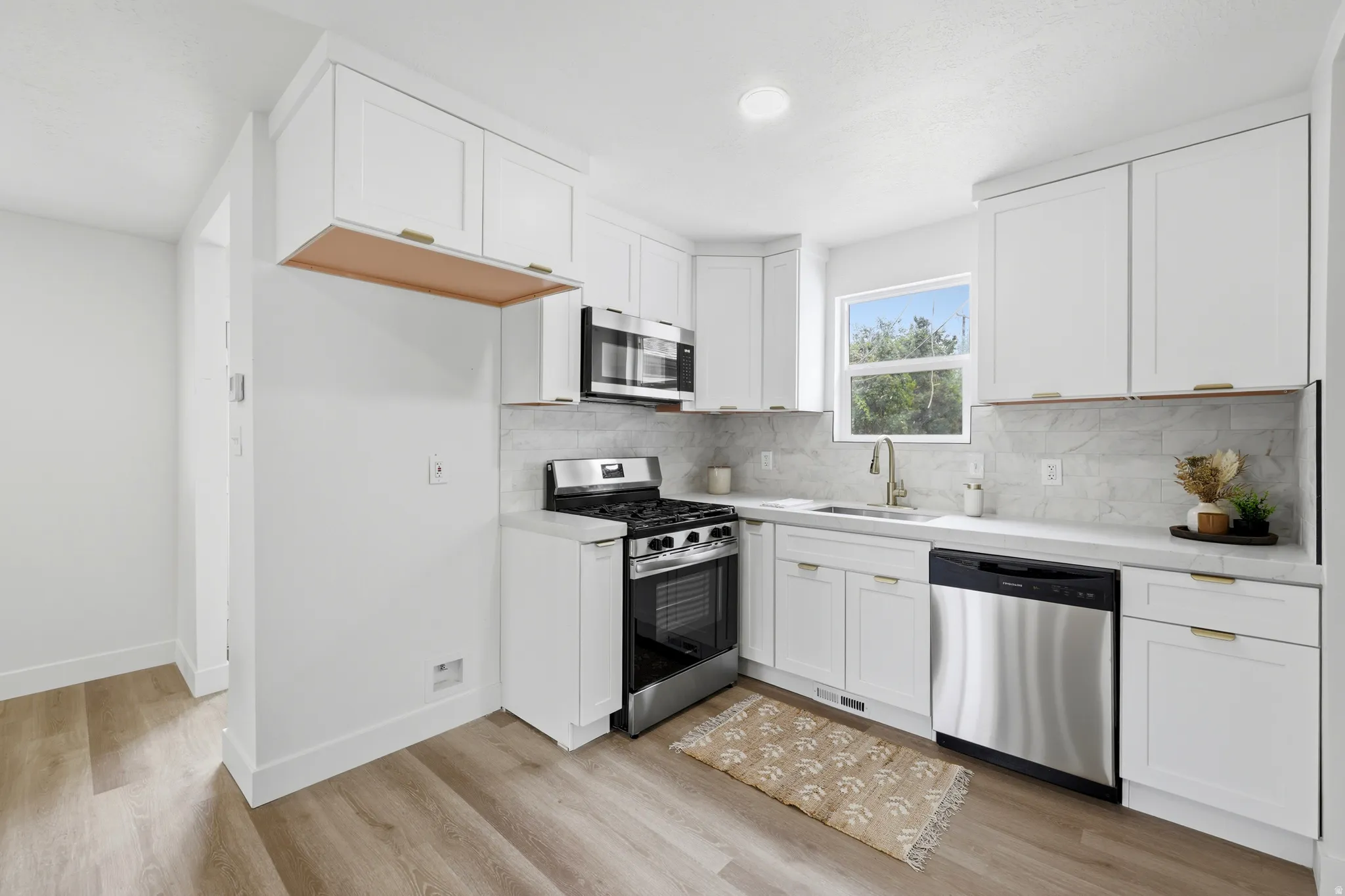 Contemporary kitchen featuring white cabinetry, stainless steel appliances, light countertops, a tiled backsplash, and wood-finish flooring