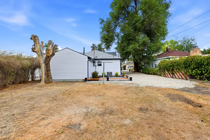 Expansive backyard featuring a white vinyl-sided exterior, a gravel driveway, mature trees, and a wooden patio area