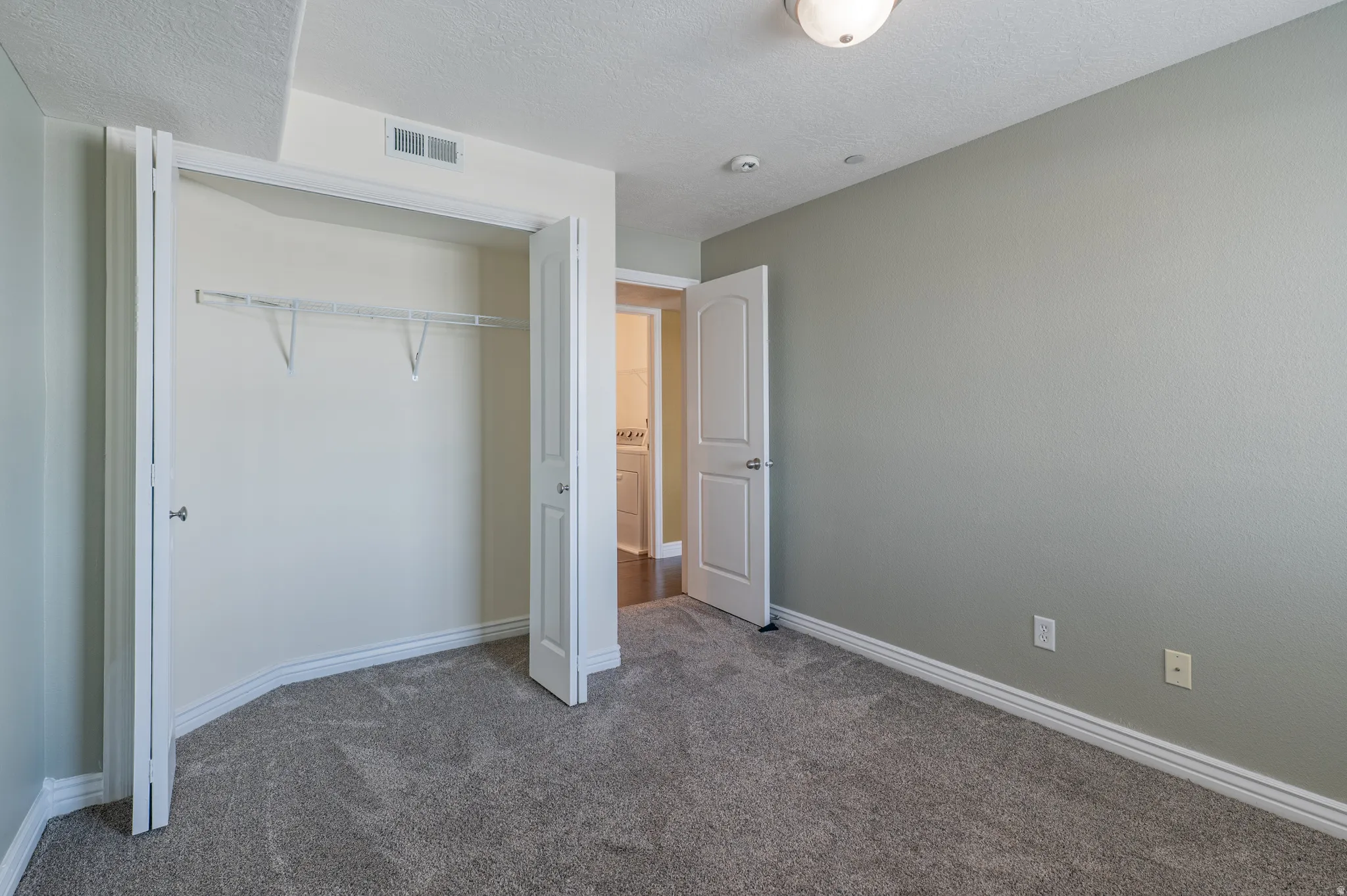 Carpeted room with a bi-fold closet, white wire shelving, and neutral wall tones