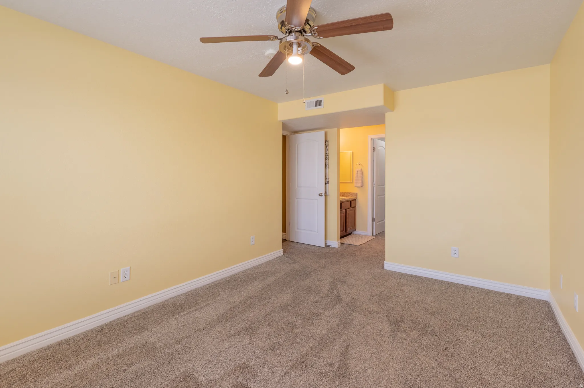 Carpeted room with a ceiling fan light fixture and an en suite bathroom featuring a single vanity with wood-finish cabinetry