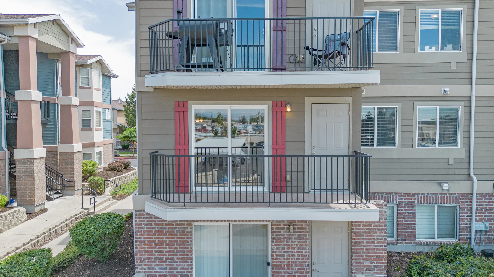 Multi-story exterior with horizontal siding, two private balconies featuring black metal railings, and red decorative shutters