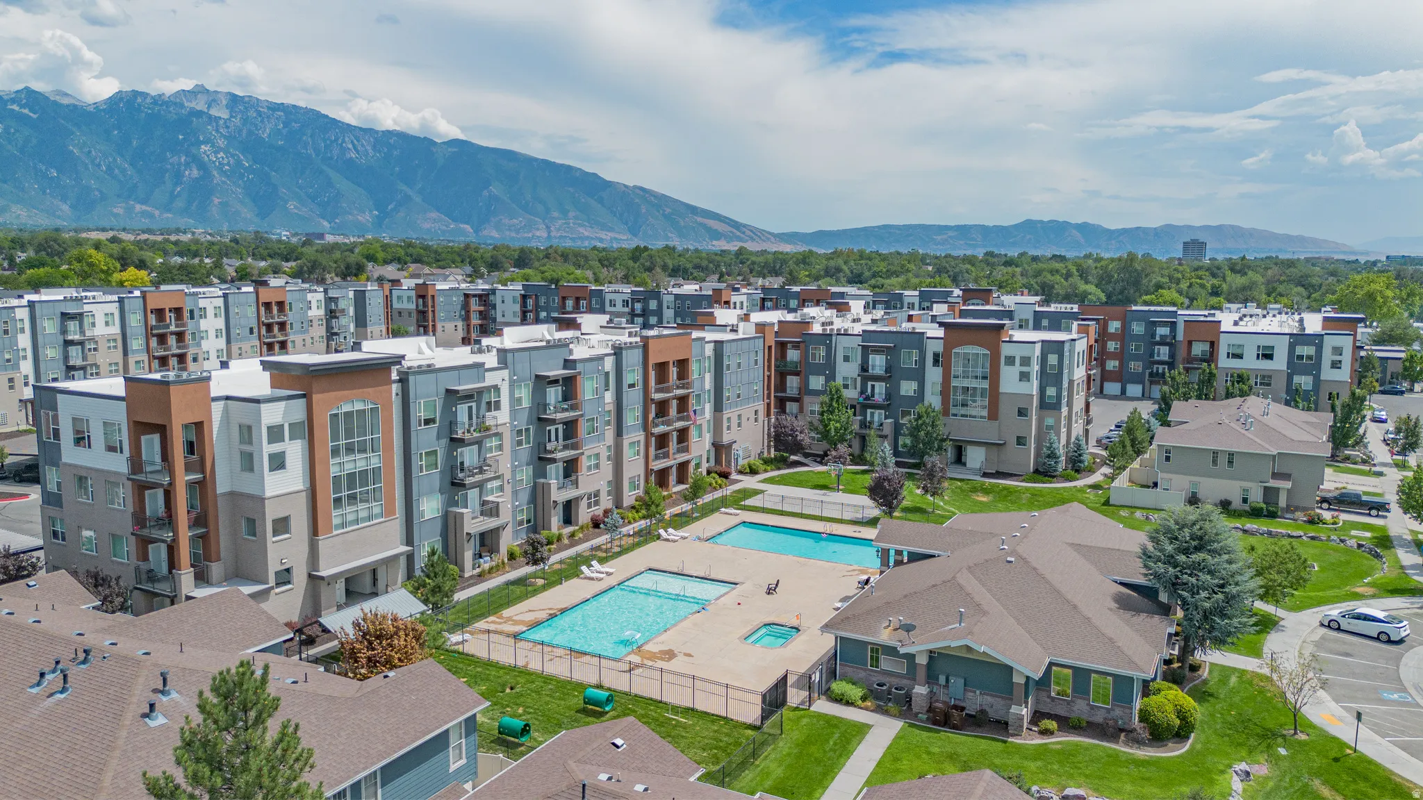 Modern apartment complex featuring multiple buildings with balconies, two outdoor swimming pools, and a separate clubhouse building