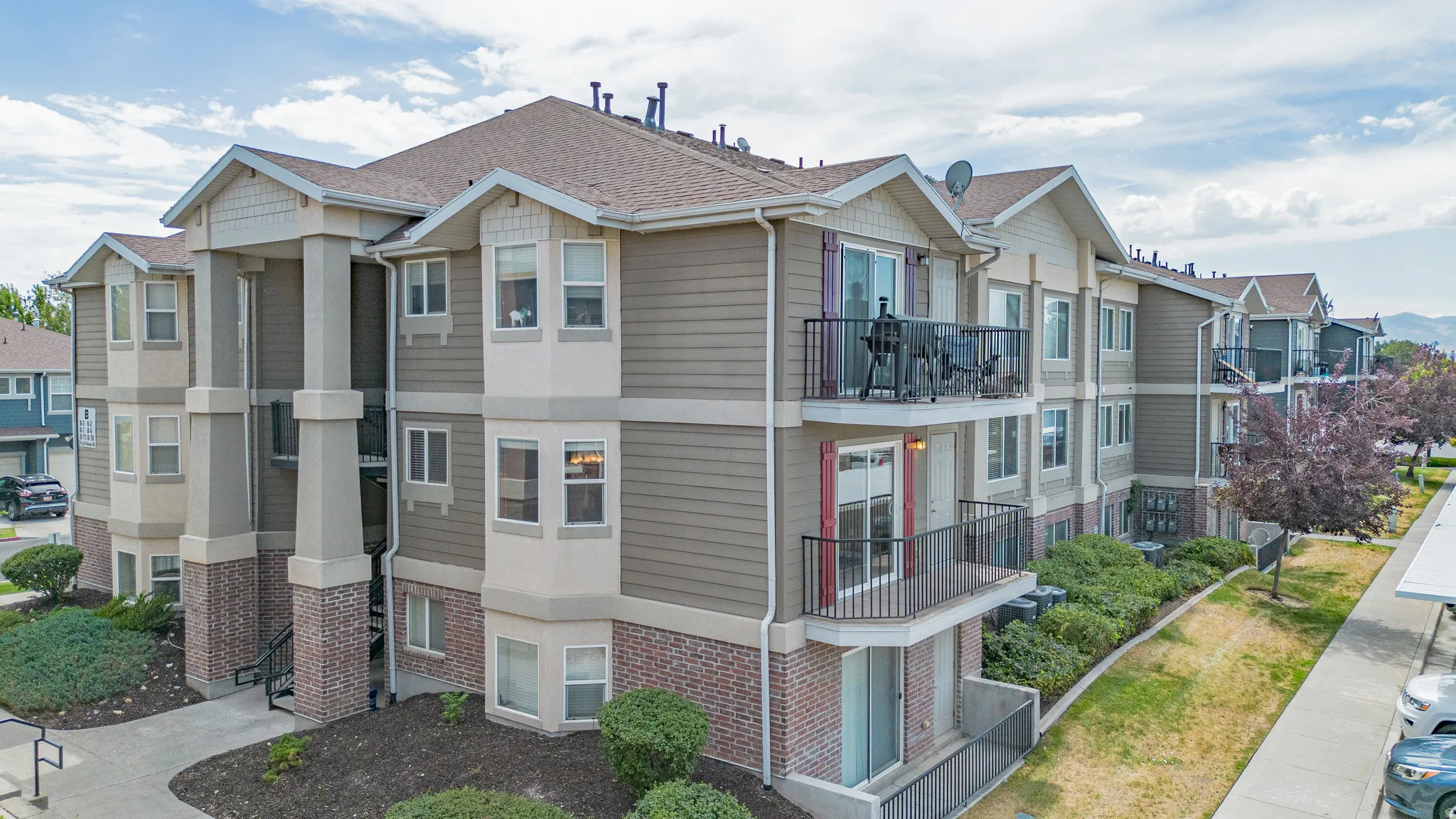 Multi-story residential building featuring balconies, bay windows, textured siding, brick accents, and a gabled roofline